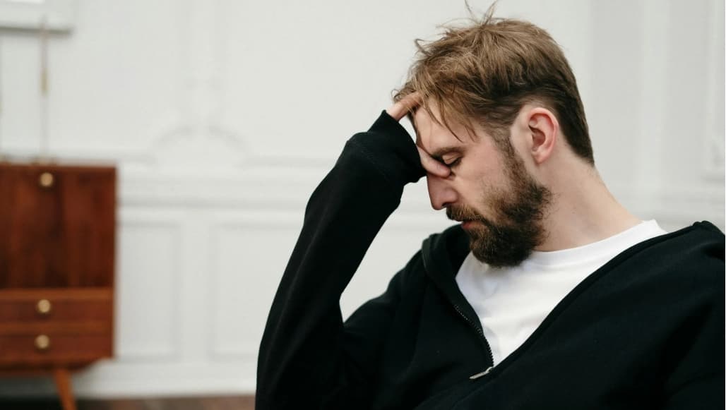 Mann med hodepine som holder seg til pannen